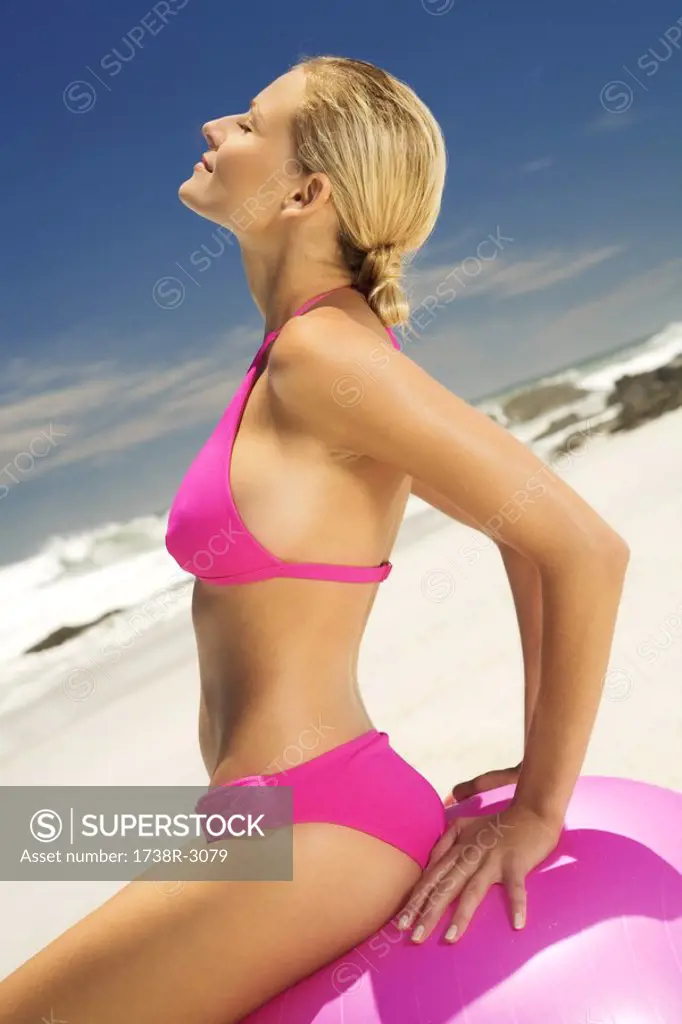 Young woman in pink bikini on the beach, sitting on a large ball