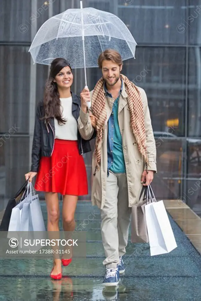 Couple with shopping bags sheltering under umbrella in rain