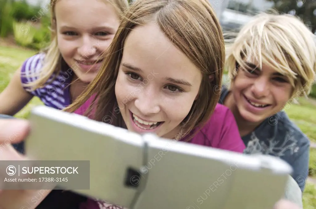 2 smiling teenage girls and boy using camera phone, outdoors
