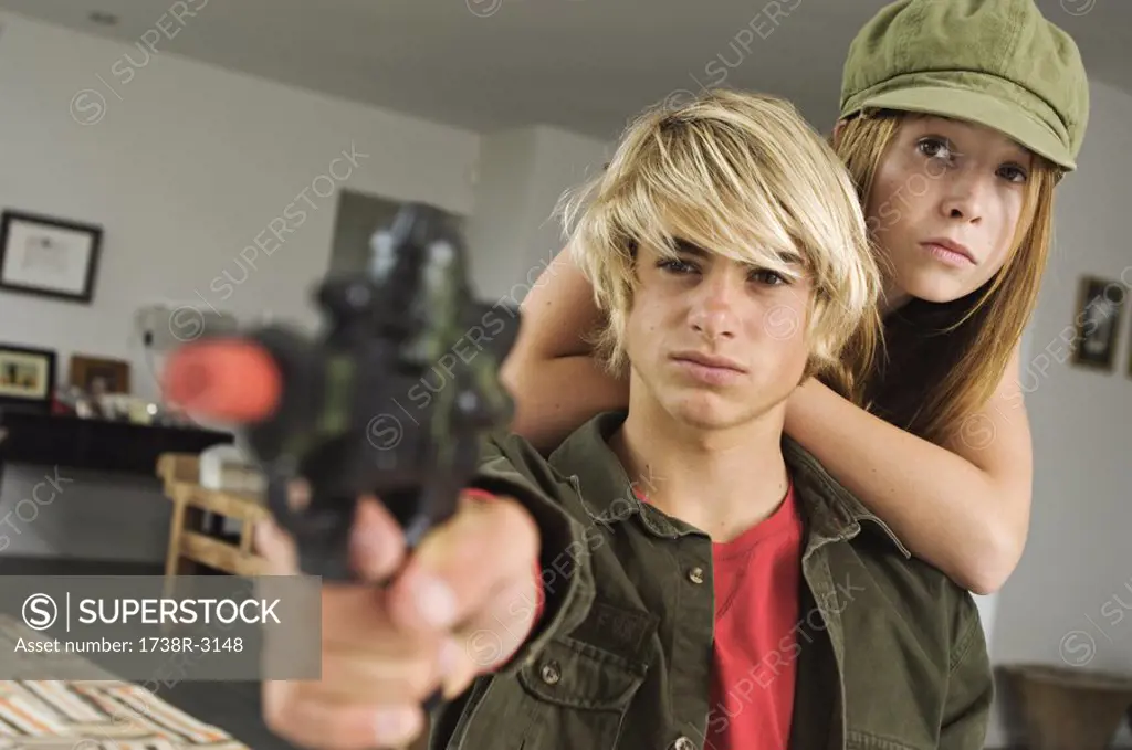 Teenage girl and boy aiming fake handgun