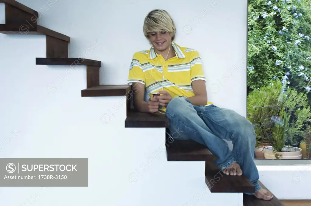 Teenage boy listening to music, sitting on stairs