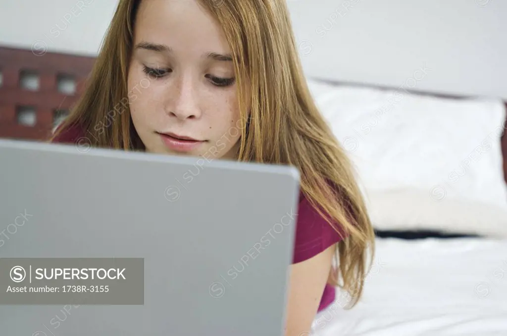 Teenage girl using laptop, lying on bed