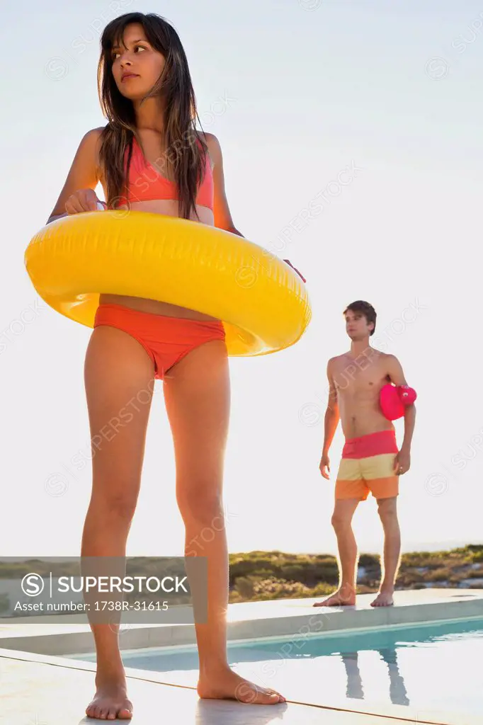 Woman walking with inflatable ring at the poolside with a man behind her