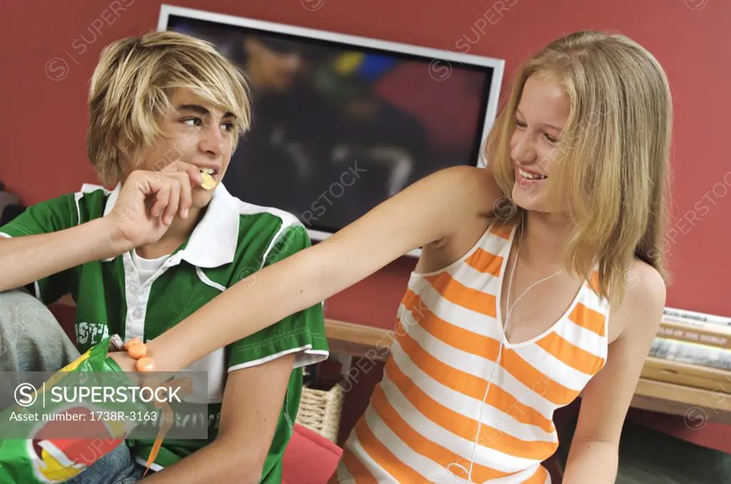 Teenage boy and girl eating crisps