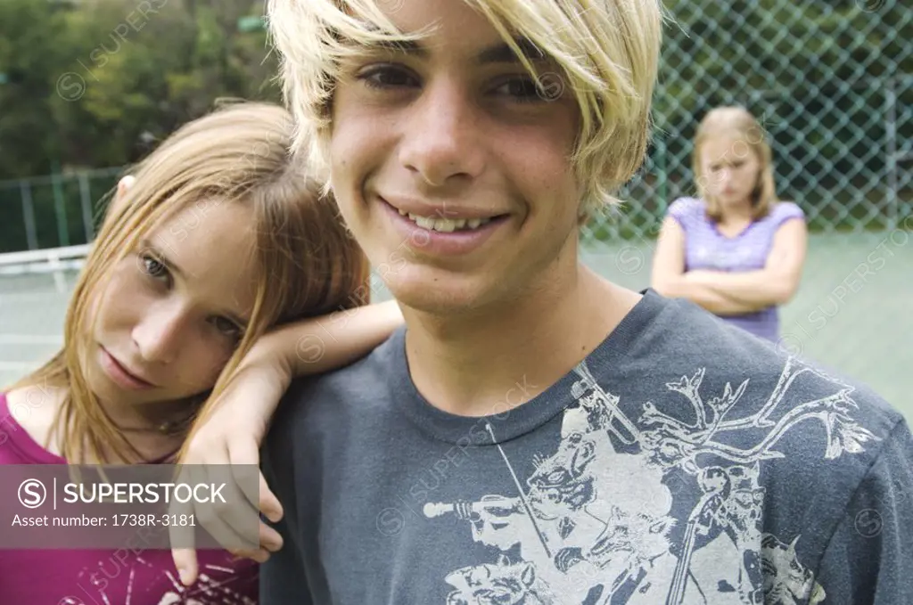 Smiling teenagers looking at the camera, teen girl with arms crossed in background, outdoors