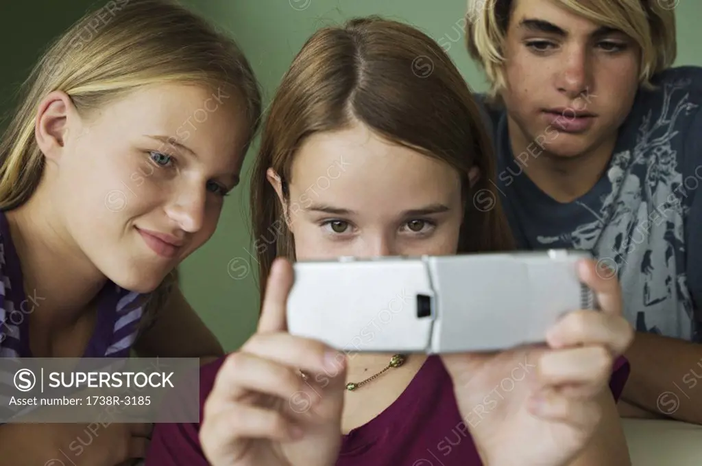 2 teenage girls and boy using camera phone