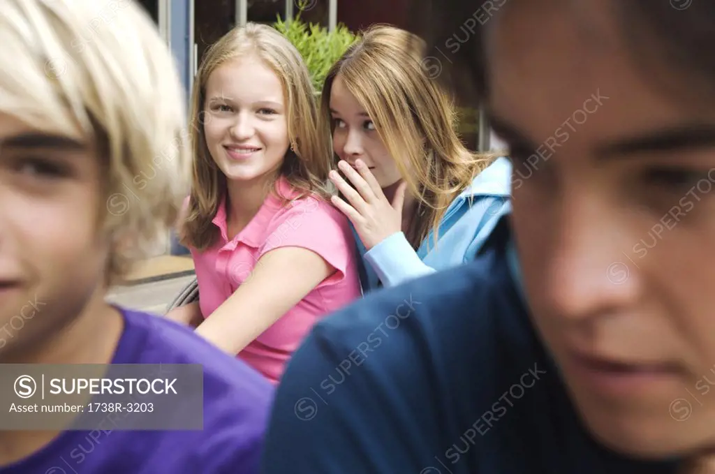 2 teenage girls whispering secrets, 2 teenage boys in foreground