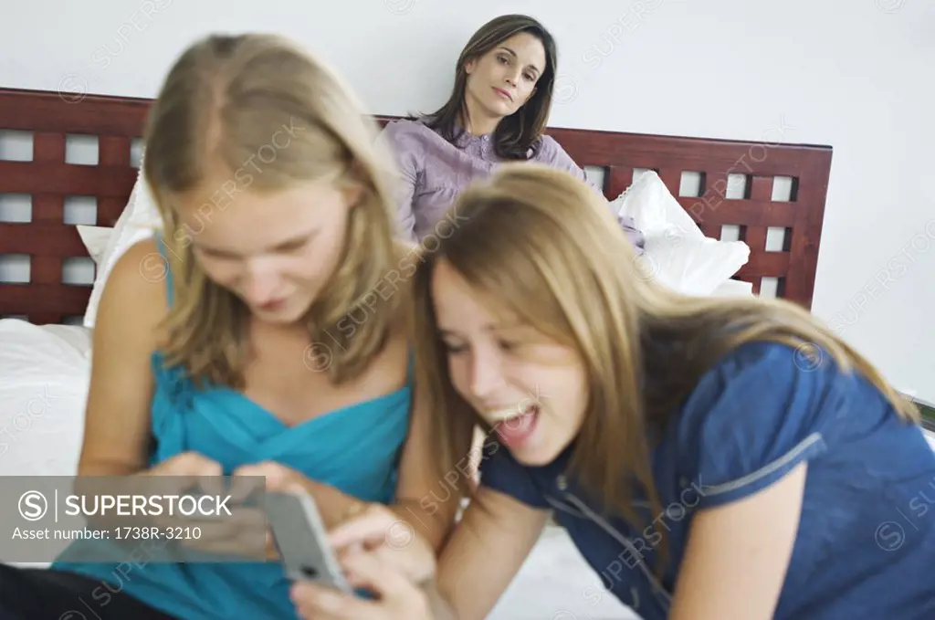 2 smiling teenage girls using mobile phones, woman in background
