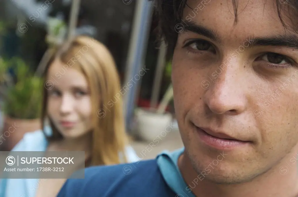 Portrait of a teenage boy looking at the camera, teenage girl in background