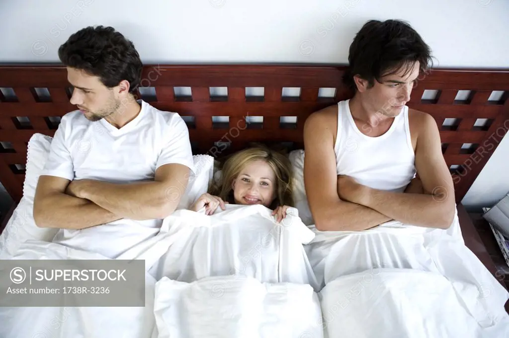 Young smiling woman in bed between 2 men, arms crossed