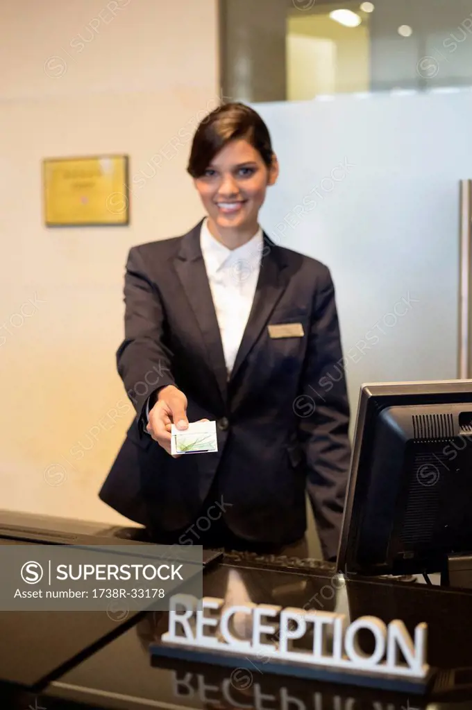 Receptionist holding a key card and smiling at the hotel reception counter