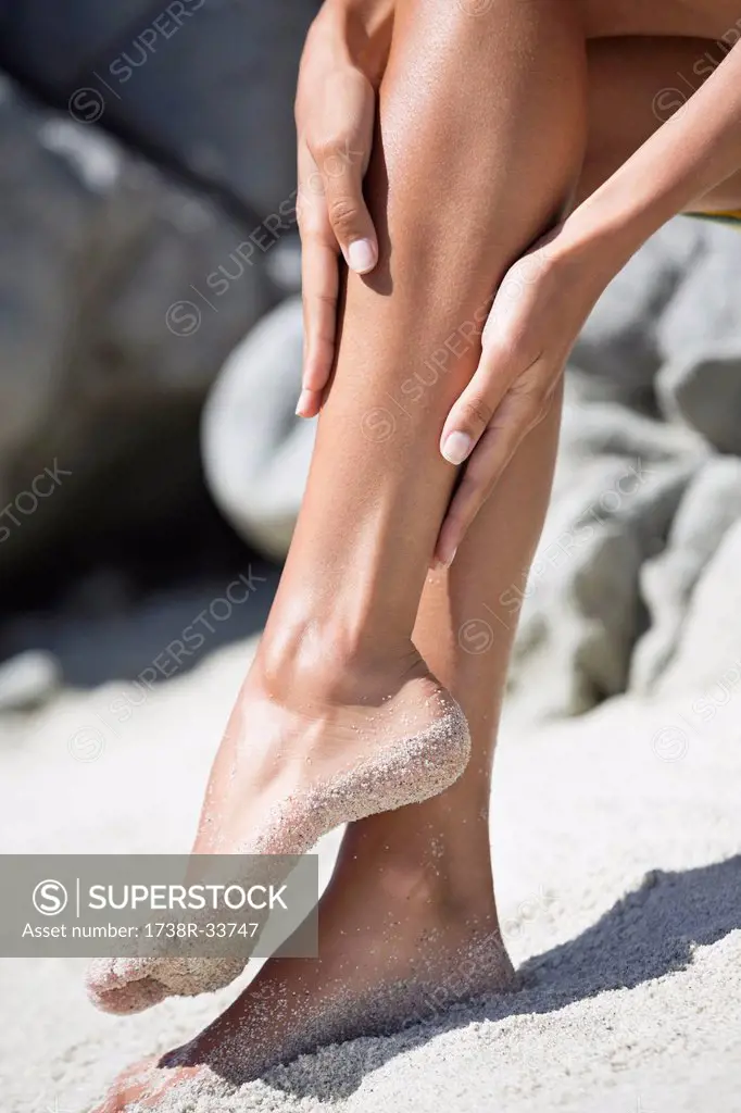 Woman applying suntan lotion on her leg on the beach