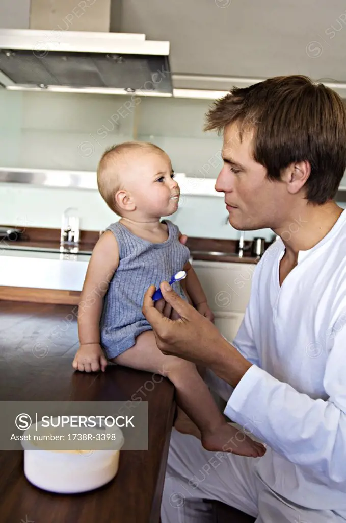 Father and son in kitchen, man feeding his baby, indoors
