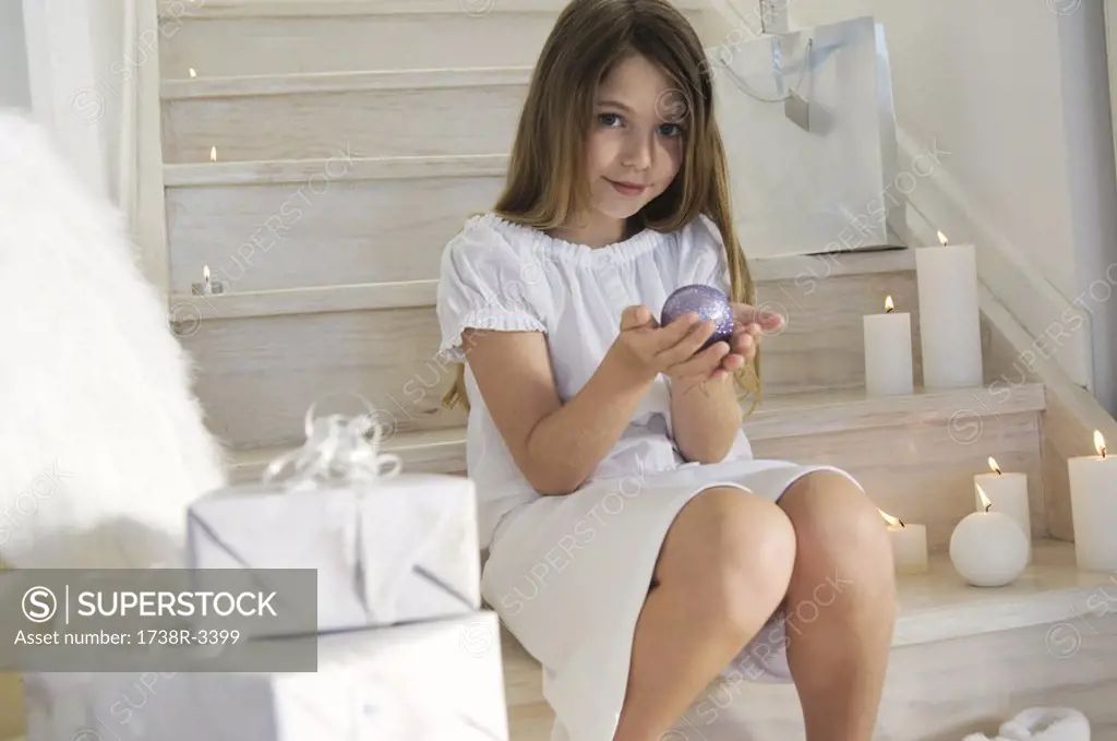 Little girl sitting indoors, holding a Christmas ball, indoors