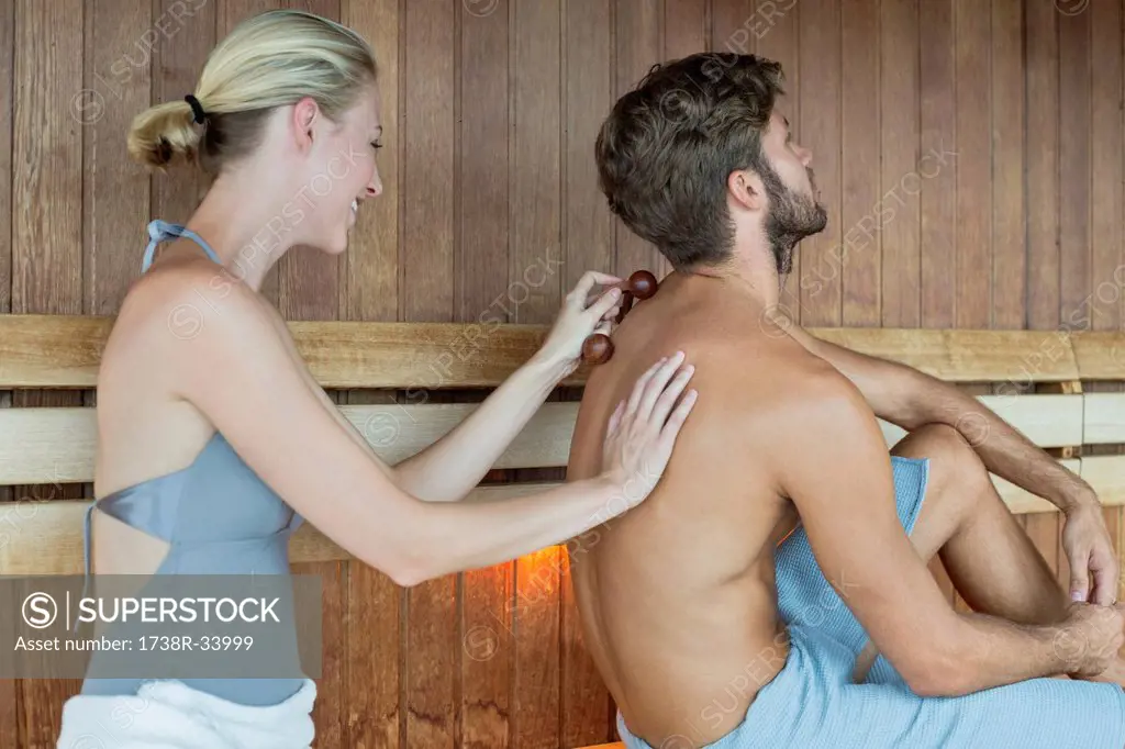 Woman massaging on her friend's back with a massager in a sauna