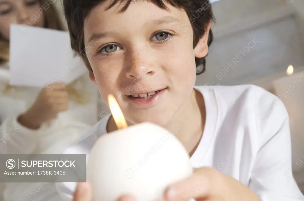 Portrait of a little boy holding a candle, sister in background, indoors