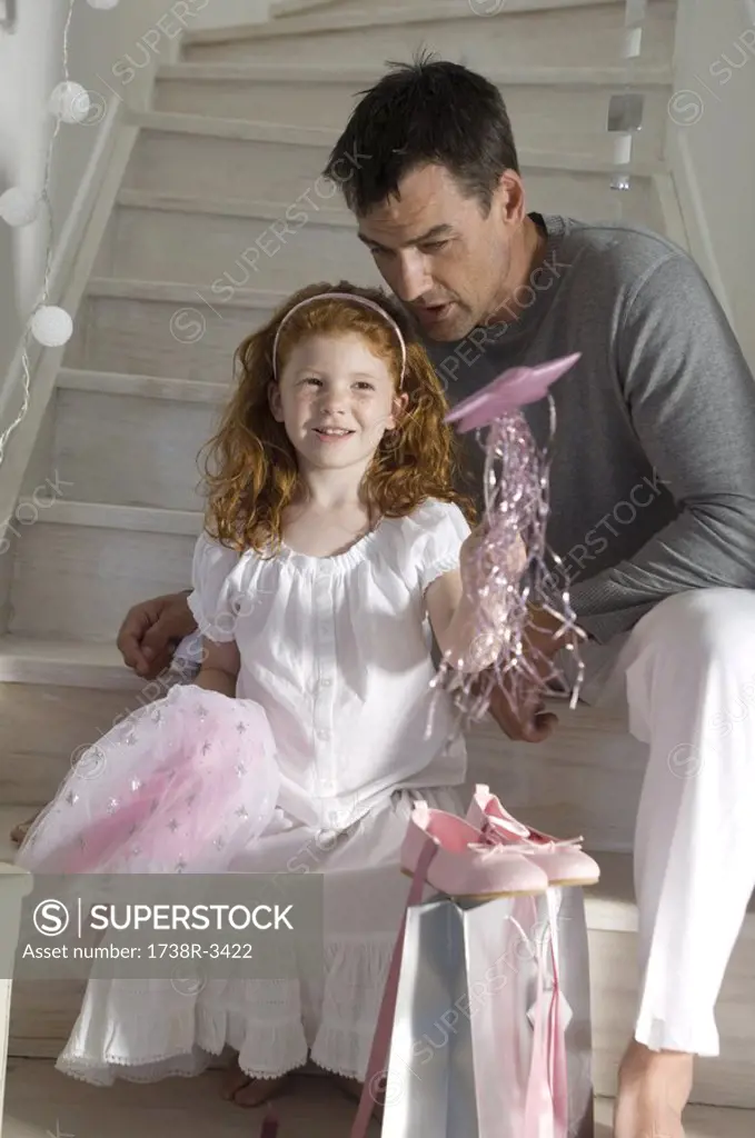Father and daughter with Christmas presents, girl holding a princess costume, indoors
