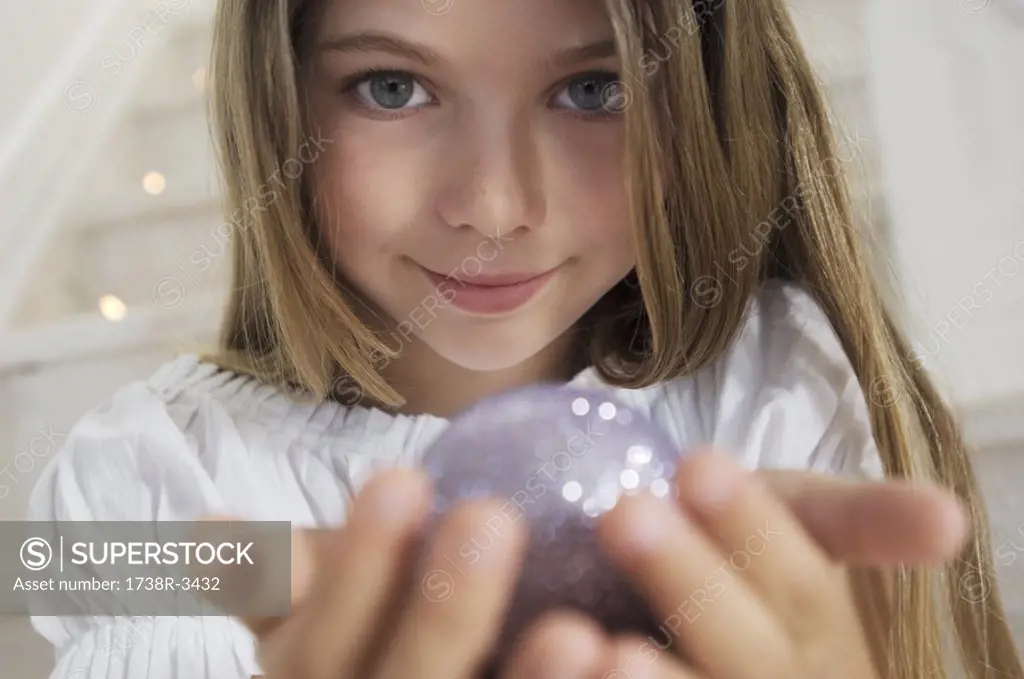 Portrait of a little girl posing for the camera, holding a Christmas ball, indoors