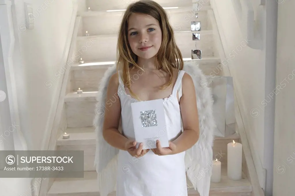Little girl in an angel costume, holding a Christmas card, indoors