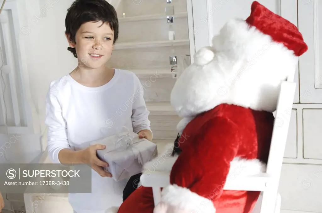 Little boy holding a present, looking at a cuddly toy Santa Claus, indoors