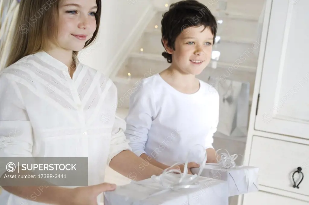 Lillte girl and little boy offering Christmas presents, indoors