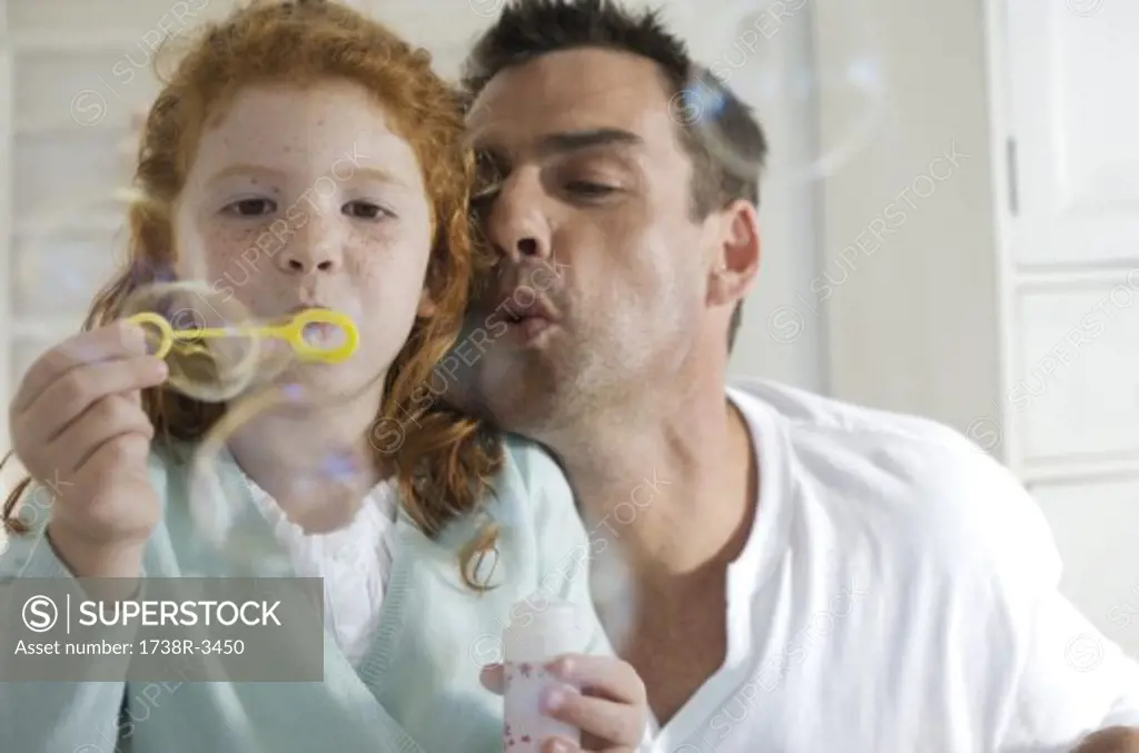 Father and daughter making soap bubbles, indoors