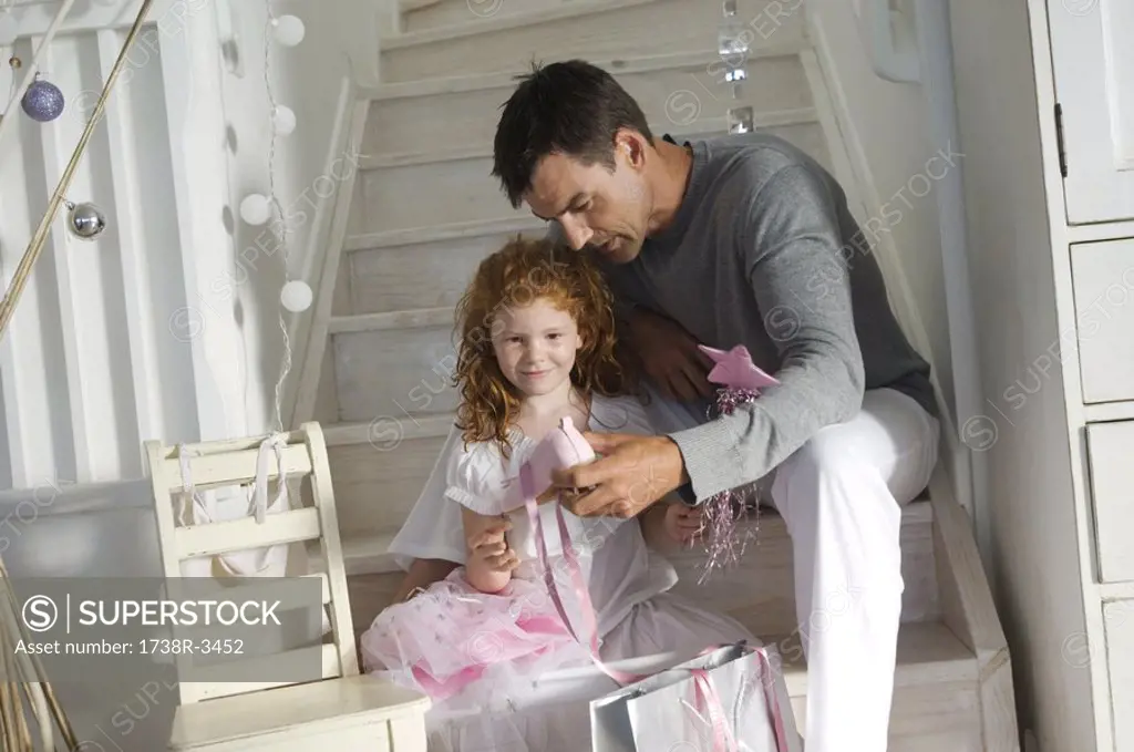 Father and ldaughter opening Christmas presents, girl holding a princess costume, indoors