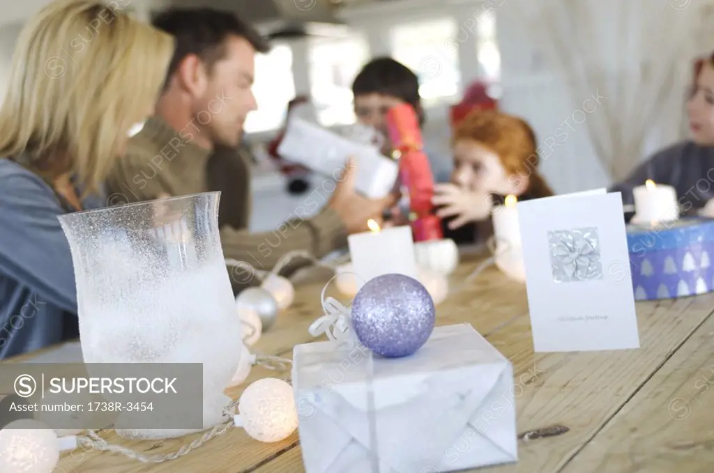 Couple and three children sitting around table, exchanging Christmas presents, indoors