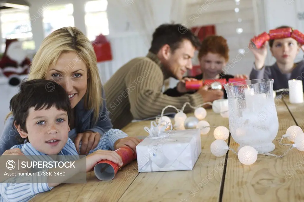 Couple and three children sitting around table, exchanging Christmas presents, indoors