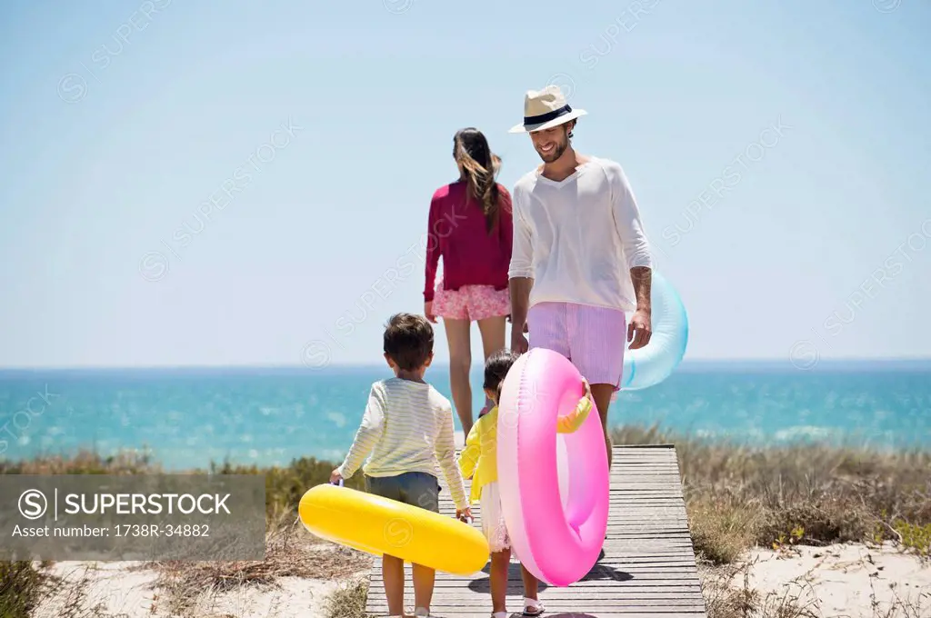 Children with their parents holding inflatable rings on a boardwalk on the beach