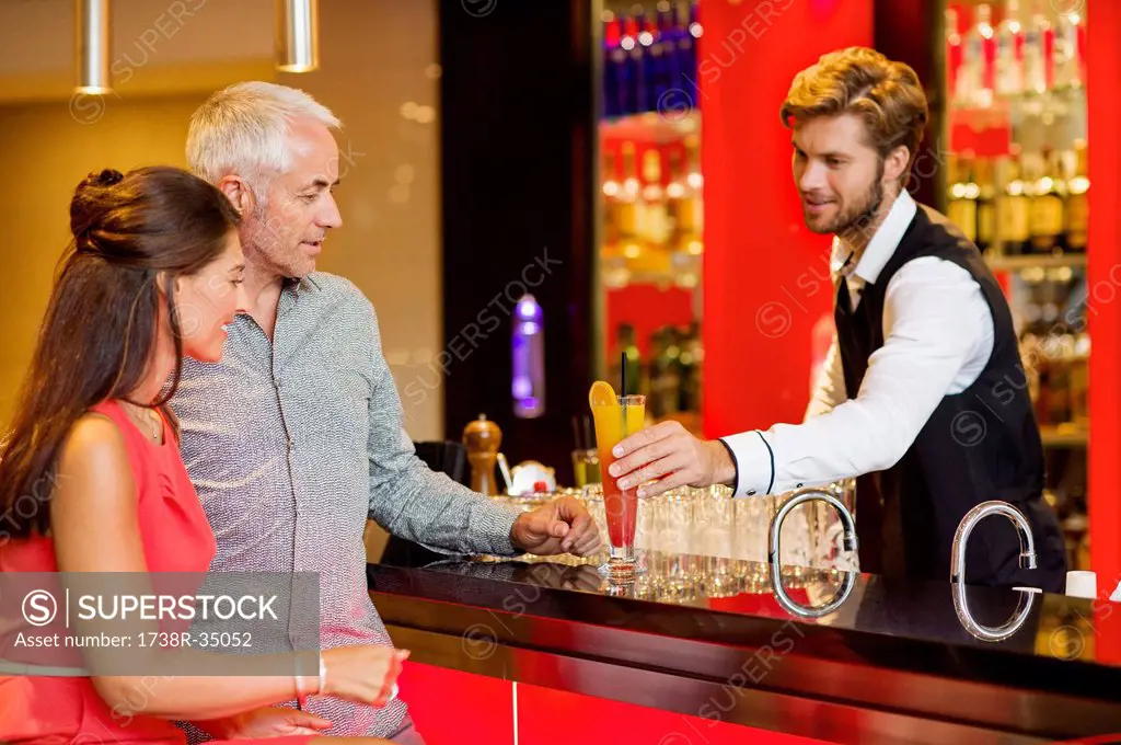 Bartender serving drink to a couple at bar counter