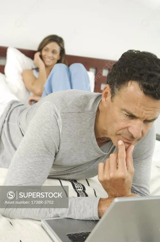 Couple in bedroom, man using laptop, indoors