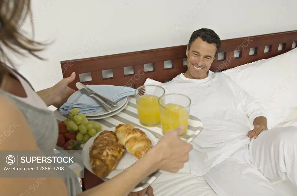 Woman bringing breakfast to man lying on bed, indoors