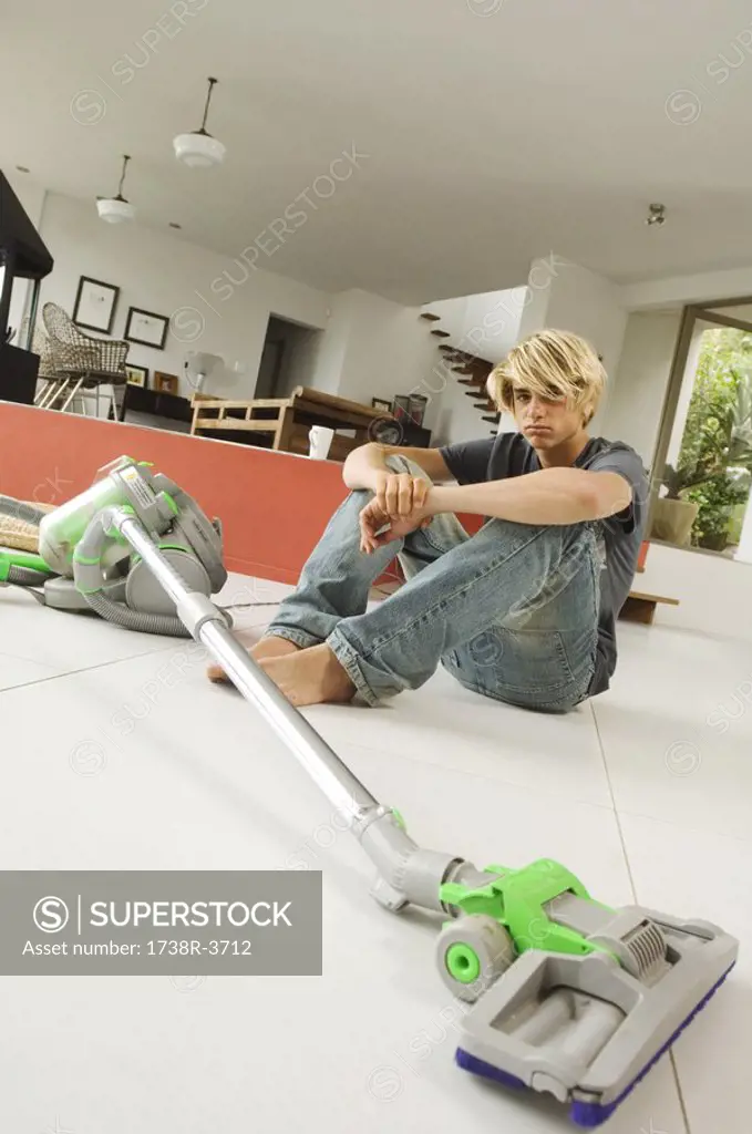 Teenager sitting on floor in living room, vacum cleaner, indoors