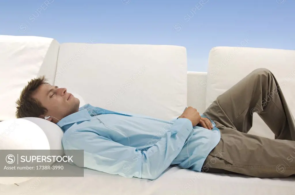 Young man listening to MP3 player lying on sofa