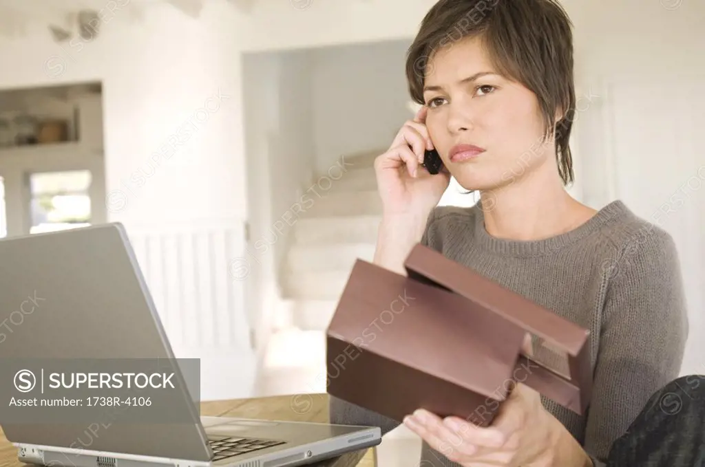 Young woman with laptop, phoning, holding box