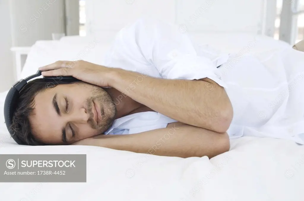 Young man listening to music with headphones, lying on bed