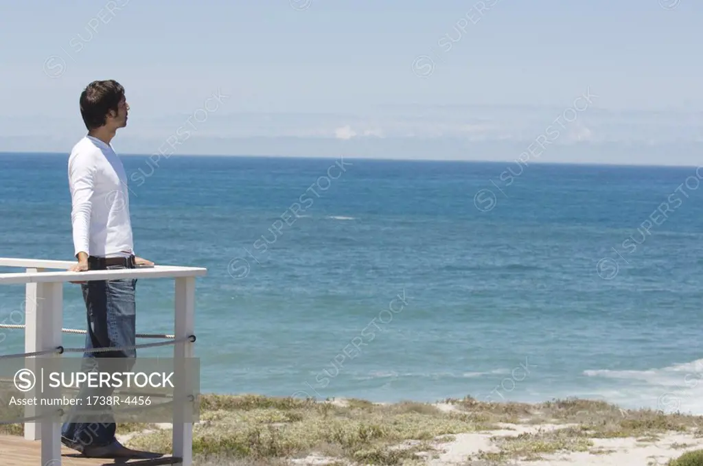 Young man leaning against balustrade, looking out to sea