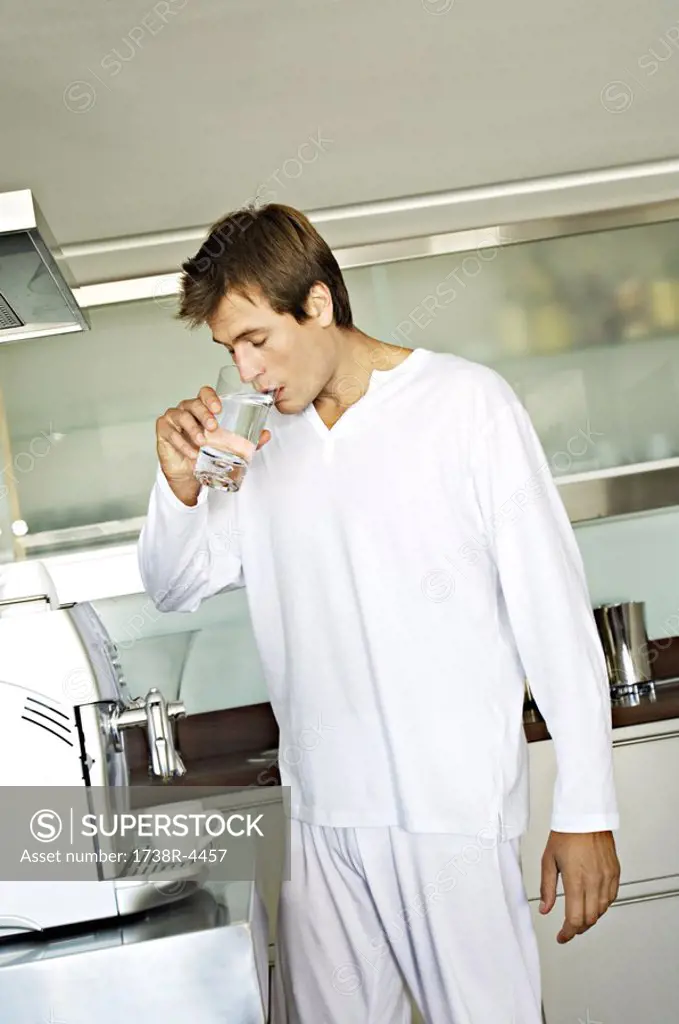 Young man drinking water in kitchen