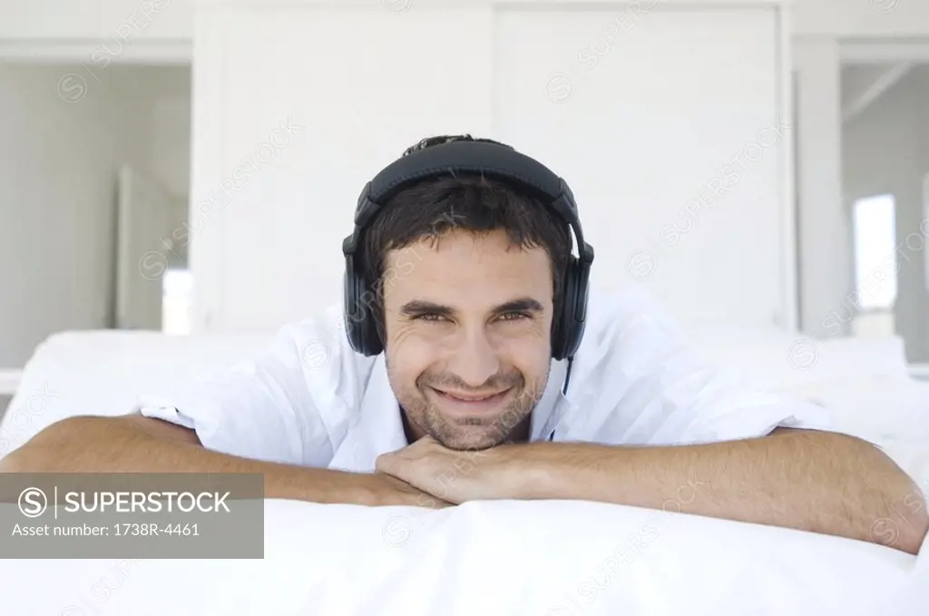 Young smiling man lying on bed, listening to music with headphones