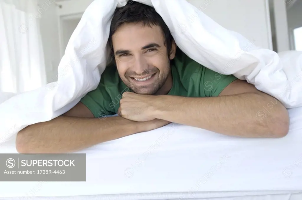 Young smiling man lying under duvet