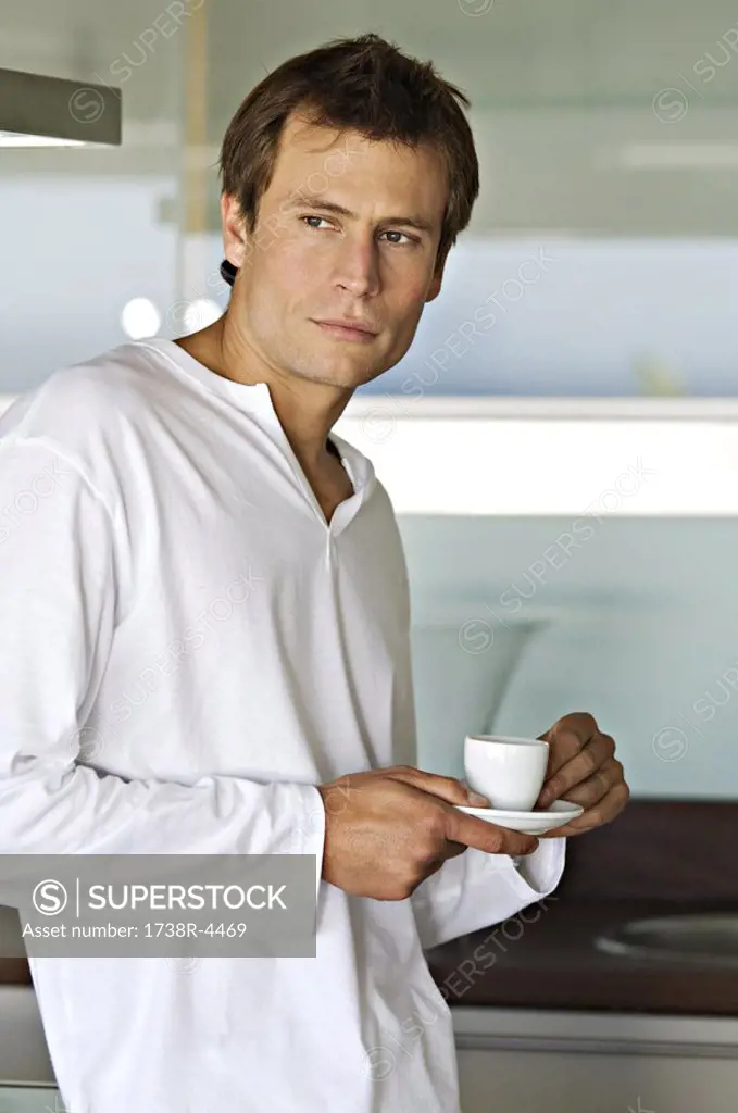 Young thinking man in kitchen, holding coffee cup