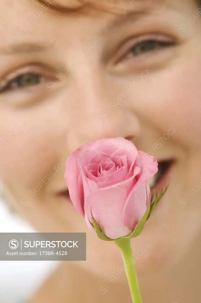 Portrait of young smiling woman with rose in front of face