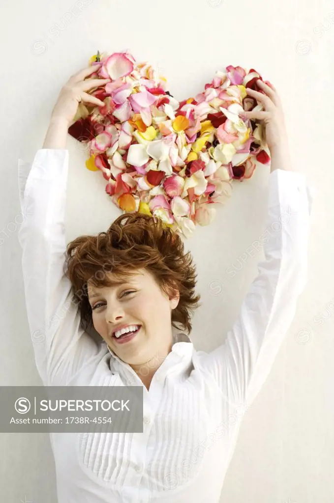 Portrait of young smiling woman holding flowers petals in heart shape