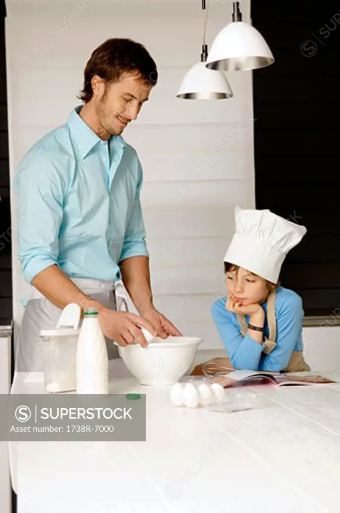 Mid adult man making a cake and his son in the kitchen
