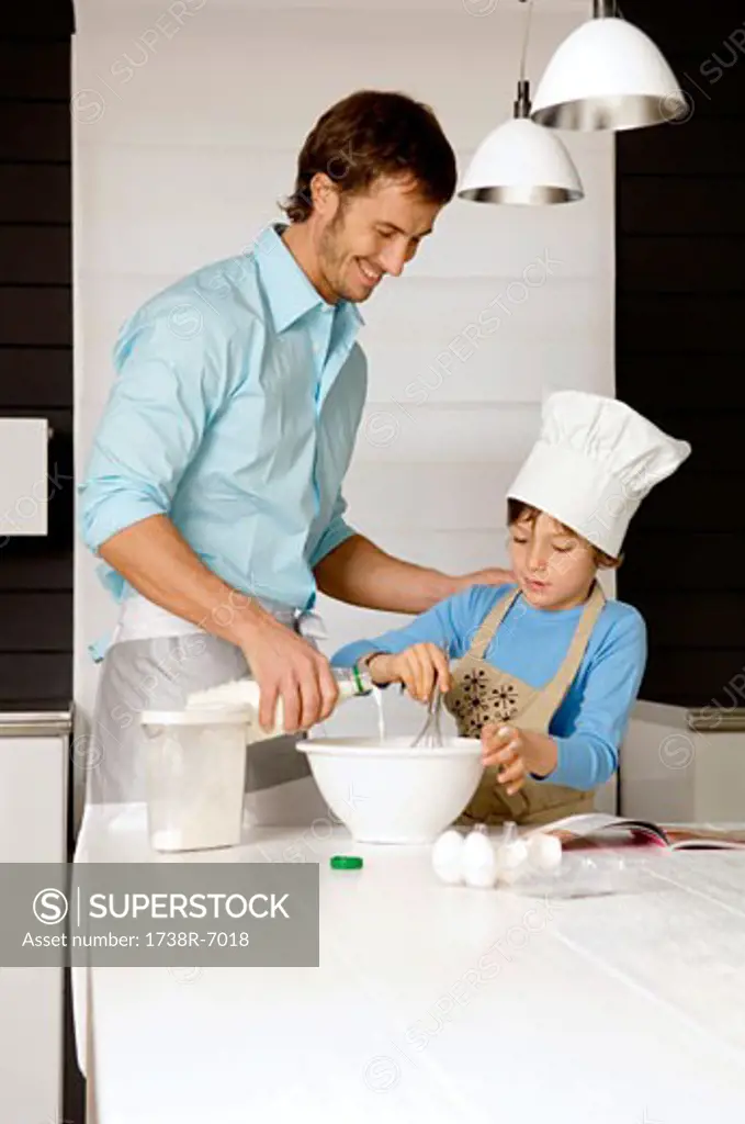 Mid adult man making a cake with his son in the kitchen