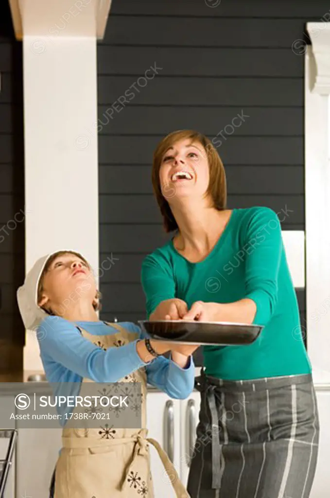 Young woman holding a frying pan with her son and smiling