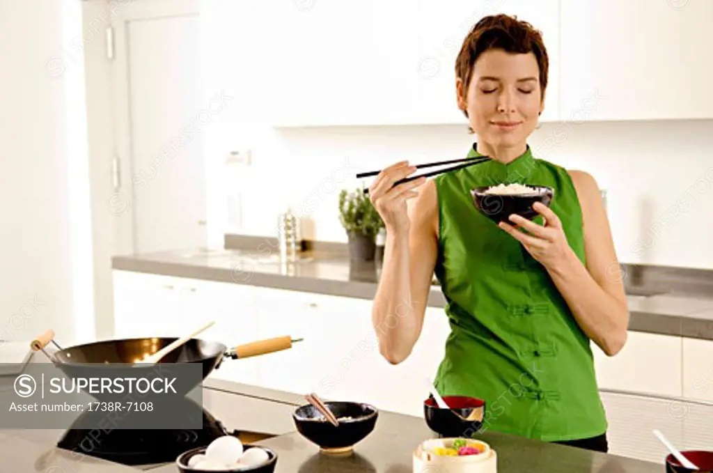 Mid adult woman smelling a bowl of rice in the kitchen