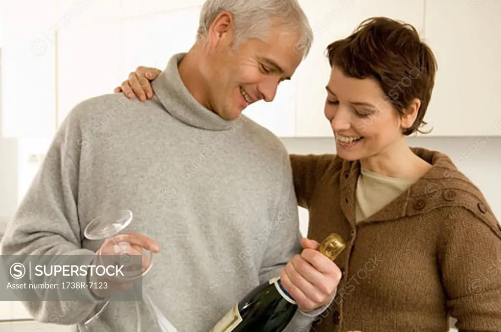 Mature man and a mid adult woman looking at a champagne bottle