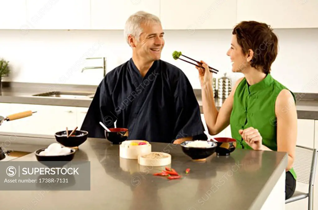 Mid adult woman feeding food to a mature man in the kitchen